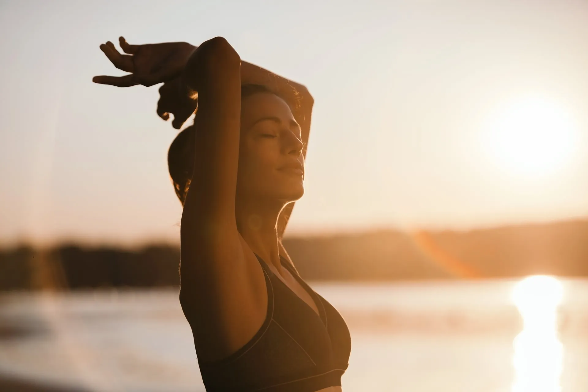 Sportliche Frau dehnt sich im Morgenlicht am Wasser