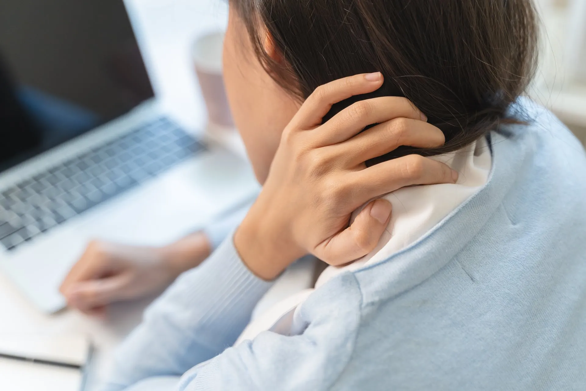 Person am Laptop greift sich an den verspannten Nacken